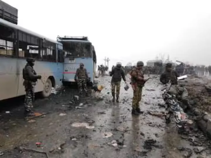 Aftermath of a roadside explosion: a heavily damaged bus, scattered debris across the road, and Indian security personnel examining the site.