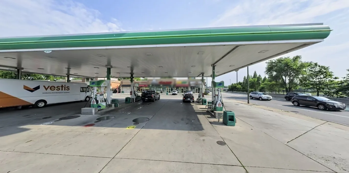 The challenge photo: a bp canopy seen from underneath, a white Vestis van at the pumps on the left, a strip mall with blurred signs in the middle, and a multi-lane road with a concrete wall and trees on the right