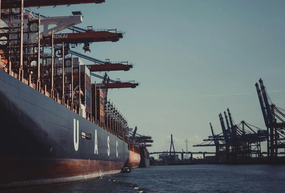 The challenge photo: the dark hull of a container ship with the white letters U A S C on the left, red gantry cranes reaching over the deck, a row of blue-and-red container cranes on the right, and a cable-stayed bridge on the horizon in the middle