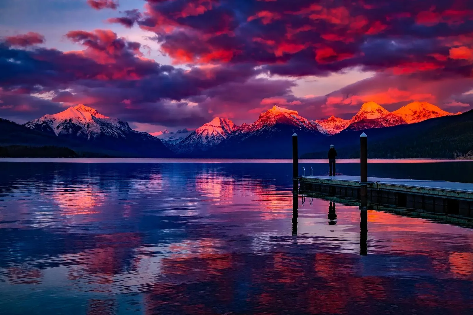 The challenge image: a mountain lake at sunset, red and violet clouds above snow-covered peaks lit orange, a calm reflecting lake, and on the right a wooden dock with two posts and a person standing at the end