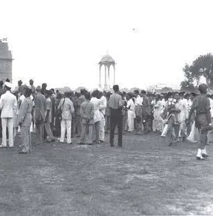 The challenge photograph: a loose crowd in light clothing on an open lawn, a monumental arch at the left frame edge, a domed canopy on columns in the background, a flagpole barely visible above the arch