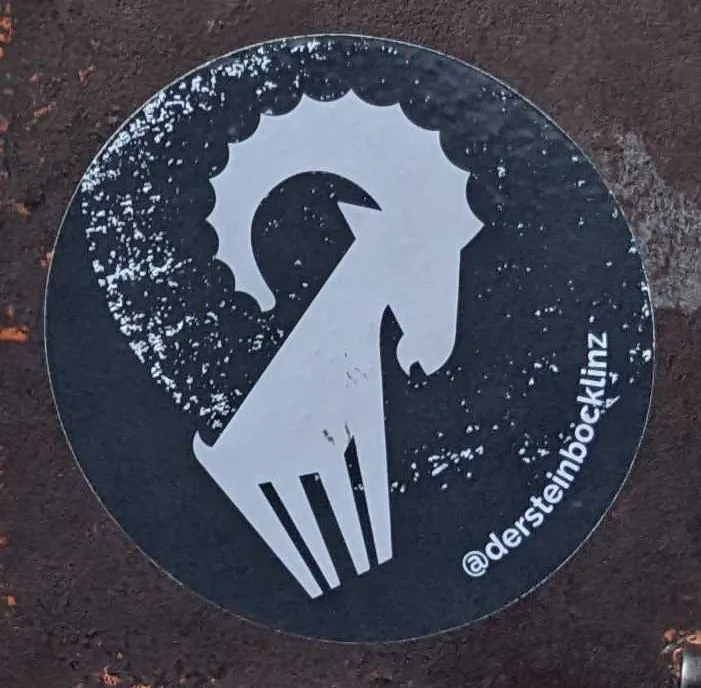 The ibex sticker cropped from the challenge: a white stylised ibex head with curved horns on a black circle, signed @dersteinbocklinz