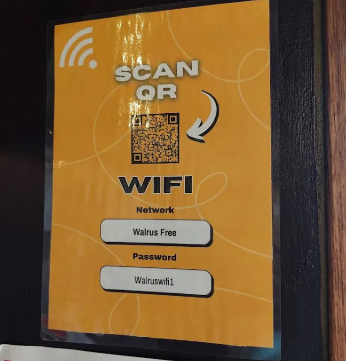 A laminated orange 'SCAN QR — WIFI' poster on the wall: Network 'Walrus Free', Password 'Walruswifi1', with a QR code above